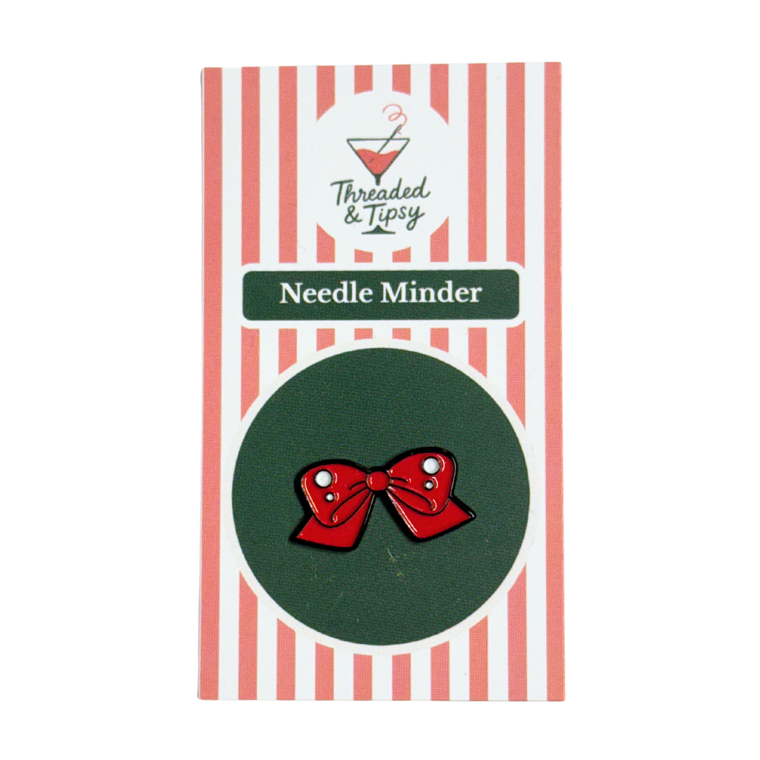 Red bow-shaped needle minder on green background with striped packaging