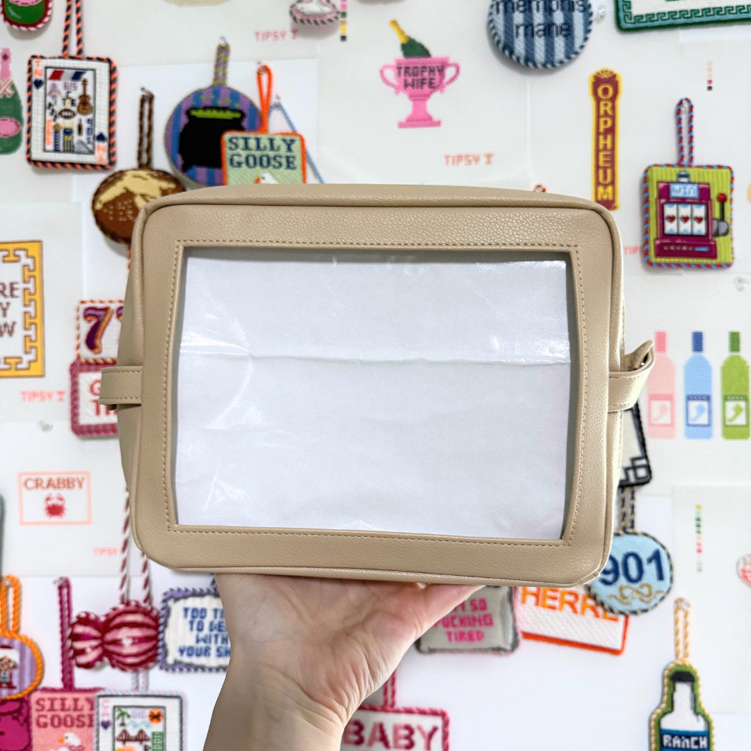 Beige needlepoint self-finishing pouch held in front of a colorful background with various designs and text.