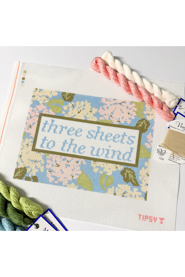 Needlepoint Kit project with 'three sheets to the wind' text and floral design, surrounded by yarn and threads.