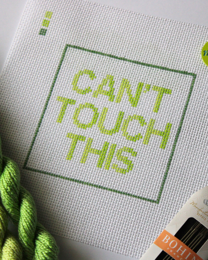 Threaded & Tipsy hand-painted needlepoint canvas featuring the phrase “CAN’T TOUCH THIS” in bold gradient lime and yellow-green block letters, framed by a green rectangular border. A small painted color guide with three green shades appears in the top left corner. Surrounding the canvas are twisted skeins of green needlepoint threads, a pack of Bohin embroidery needles in the bottom right, and a round lime green enamel pin in the top right corner that reads “ndlpt MAFIA.” 