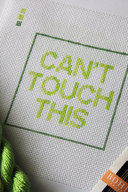 Threaded & Tipsy hand-painted needlepoint canvas featuring the phrase “CAN’T TOUCH THIS” in bold gradient lime and yellow-green block letters, framed by a green rectangular border. A small painted color guide with three green shades appears in the top left corner. Surrounding the canvas are twisted skeins of green needlepoint threads, a pack of Bohin embroidery needles in the bottom right, and a round lime green enamel pin in the top right corner that reads “ndlpt MAFIA.” 
