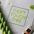 Threaded & Tipsy hand-painted needlepoint canvas featuring the phrase “CAN’T TOUCH THIS” in bold gradient lime and yellow-green block letters, framed by a green rectangular border. A small painted color guide with three green shades appears in the top left corner. Surrounding the canvas are twisted skeins of green needlepoint threads, a pack of Bohin embroidery needles in the bottom right, and a round lime green enamel pin in the top right corner that reads “ndlpt MAFIA.” 