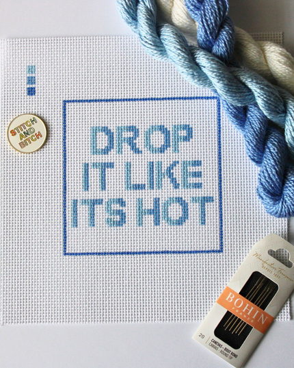 Threaded & Tipsy hand-painted needlepoint canvas featuring the phrase “HOT IN HERRE” in bold red and orange block letters, centered within a red rectangular border. A small painted color guide with four red-orange shades appears in the upper left corner. Surrounding the canvas are vibrant silk needlepoint threads in shades of red, orange, and coral, along with a pack of Bohin embroidery needles positioned at the bottom right. The canvas is unstitched and displayed on a white background.