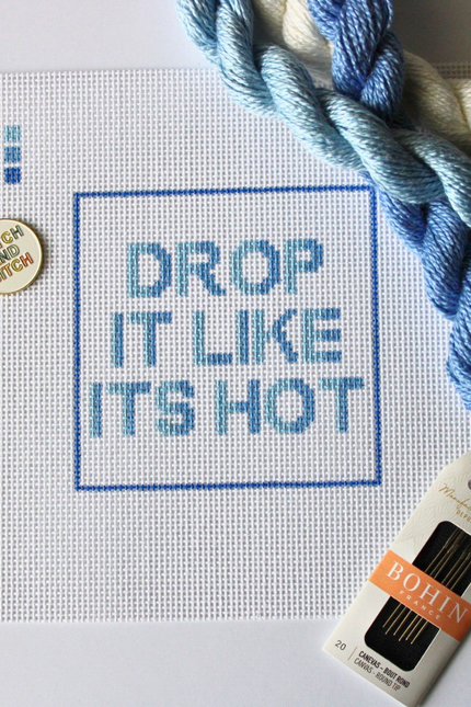 Threaded & Tipsy hand-painted needlepoint canvas featuring the phrase “HOT IN HERRE” in bold red and orange block letters, centered within a red rectangular border. A small painted color guide with four red-orange shades appears in the upper left corner. Surrounding the canvas are vibrant silk needlepoint threads in shades of red, orange, and coral, along with a pack of Bohin embroidery needles positioned at the bottom right. The canvas is unstitched and displayed on a white background.