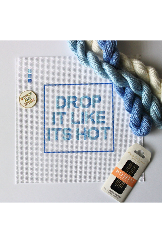 Threaded & Tipsy hand-painted needlepoint canvas featuring the phrase “HOT IN HERRE” in bold red and orange block letters, centered within a red rectangular border. A small painted color guide with four red-orange shades appears in the upper left corner. Surrounding the canvas are vibrant silk needlepoint threads in shades of red, orange, and coral, along with a pack of Bohin embroidery needles positioned at the bottom right. The canvas is unstitched and displayed on a white background.
