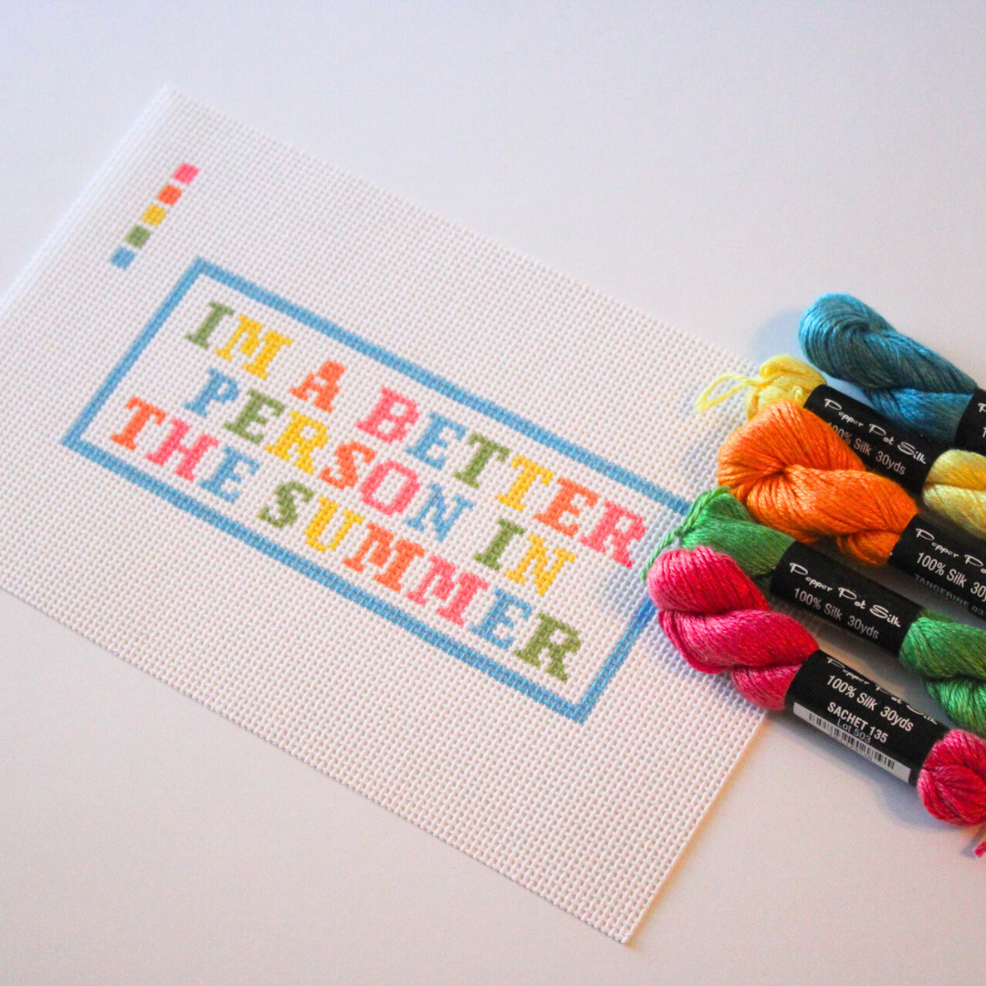needlepoint canvas with colorful text and skeins of yarn on a white background