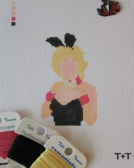 Threaded & Tipsy hand-painted needlepoint canvas featuring a faceless figure of a blonde woman in a black strapless outfit with pink gloves, a white collar, and black bunny ears. A painted color guide is visible in the upper left corner, and the initials "T+T" are painted in black in the bottom right corner. Surrounding the canvas are spools of Threaded & Tipsy needlepoint threads in pink, black, and yellow. A small enamel pin of a man in a red blazer is pinned near the top of the canvas.