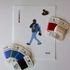 Threaded & Tipsy hand-painted needlepoint canvas featuring a pixel-style figure of a man walking while holding a phone to his ear, dressed in a black cap, black hoodie, blue jeans, and a blue and black jacket with red “RM” lettering. A painted color guide is visible on the upper left side, and the initials "T+T" are painted in black in the bottom right corner. Surrounding the canvas are Threaded & Tipsy needlepoint threads in shades of blue, black, red, and shimmery white. A small enamel pin of a man 