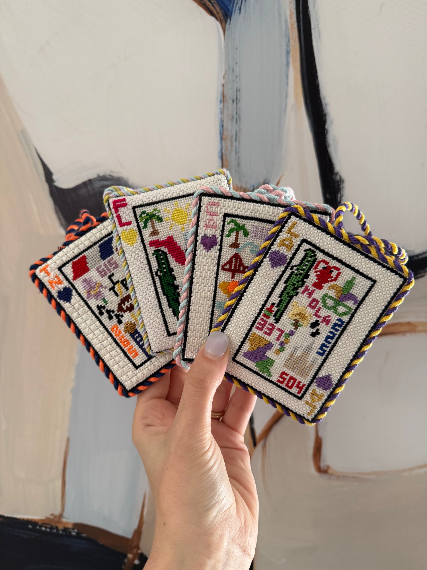 Hand holding four embroidered cards with colorful designs against a neutral background