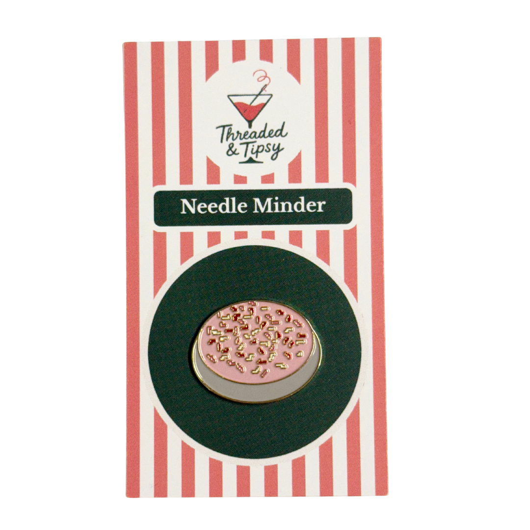 Pink needle minder with gold accents on a striped packaging by Threaded &amp; Tipsy