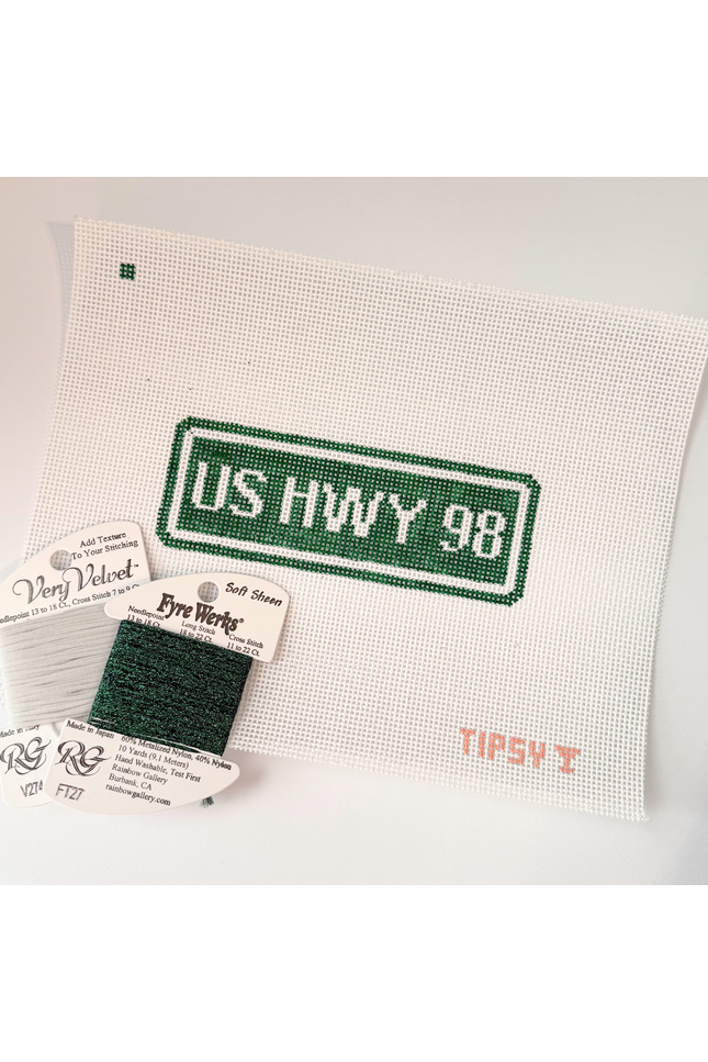 Needlepoint kit with 'US HWY 98' design on fabric, including thread labels and a swatch.