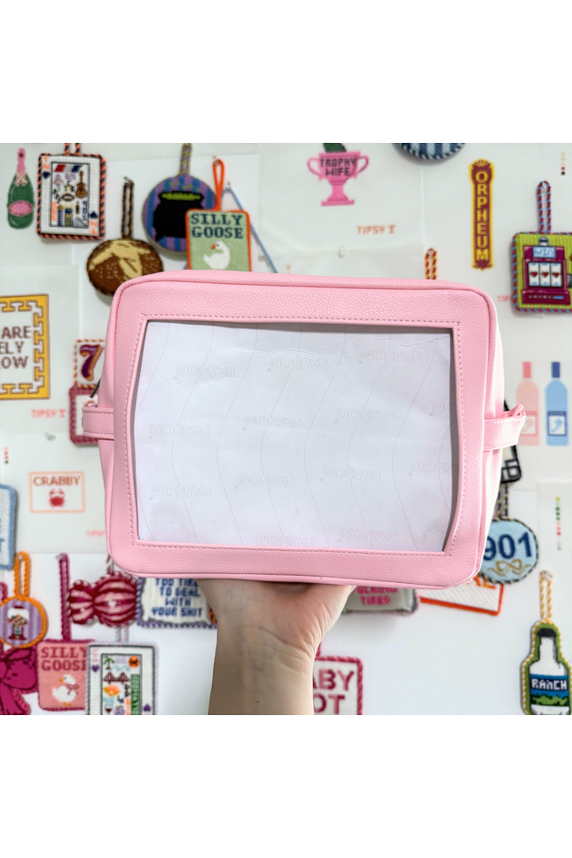 Pink self finishing needlepoint pouch in front of a colorful wall with various items.