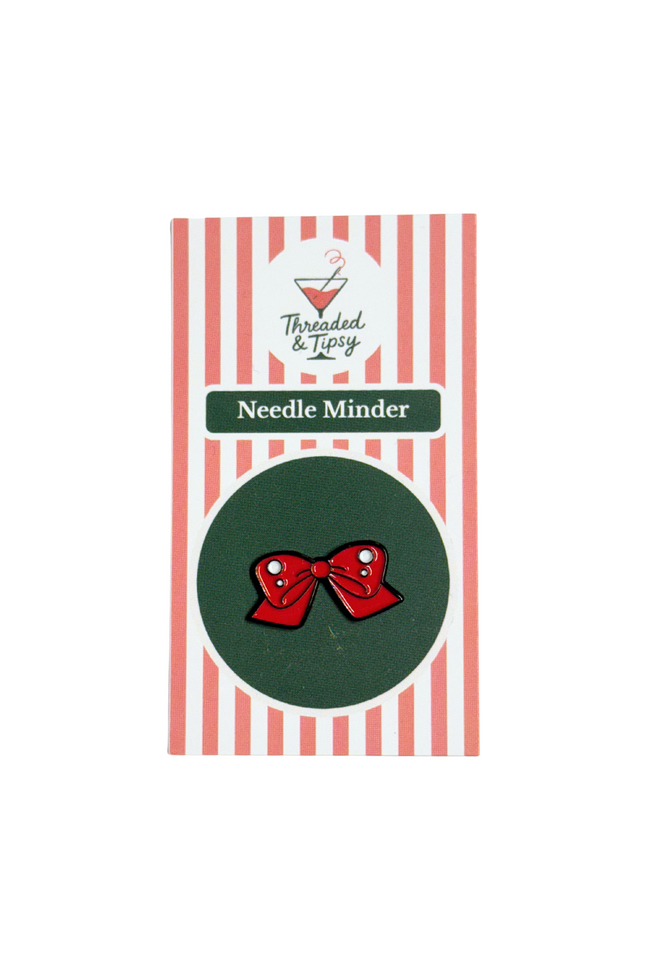 Red bow-shaped needle minder on green background with striped packaging