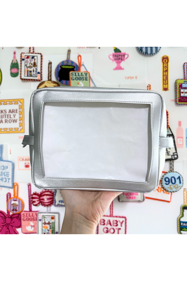 Silver self-finishing needlepoint pouch held in front of a colorful background with various text and graphics.