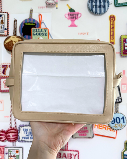 Beige needlepoint self-finishing pouch held in front of a colorful background with various designs and text.
