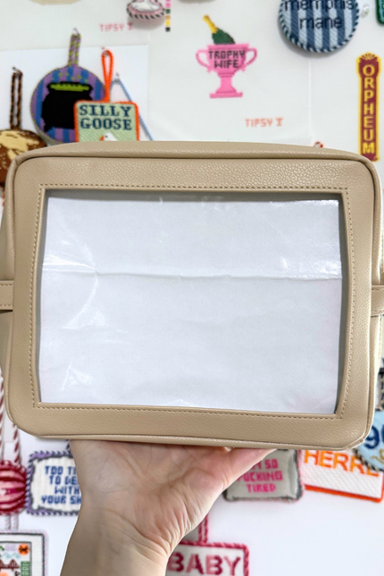 Beige needlepoint self-finishing pouch held in front of a colorful background with various designs and text.